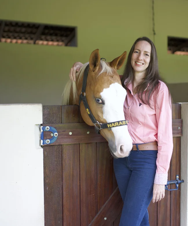 Dra. Micheline Carvalho ao lado de um cavalo na baia